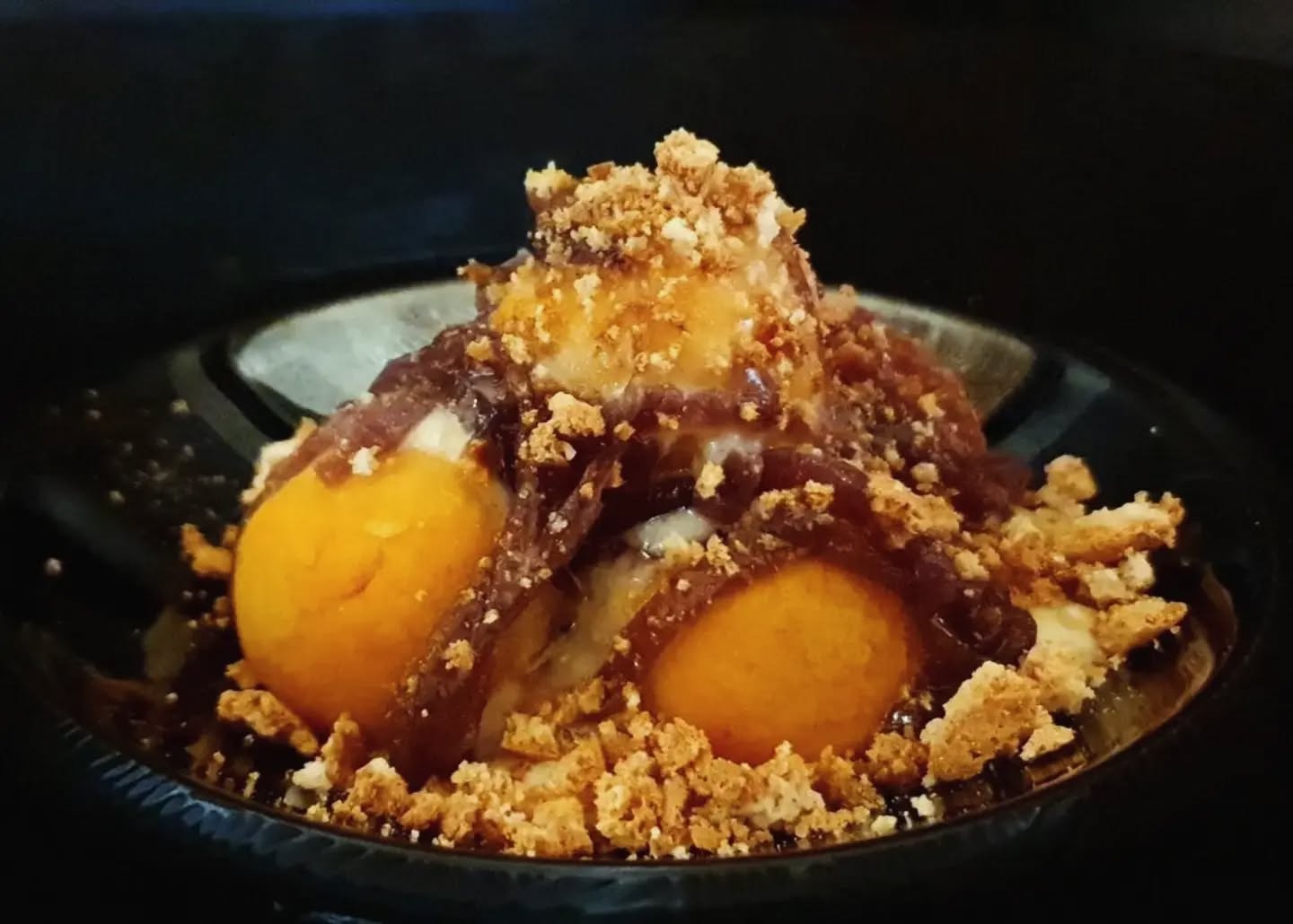 Polpette vegetariane arancioni con cipolla caramellata, crema bianca e crumble dorato in un piatto scuro, La Pecora Nera