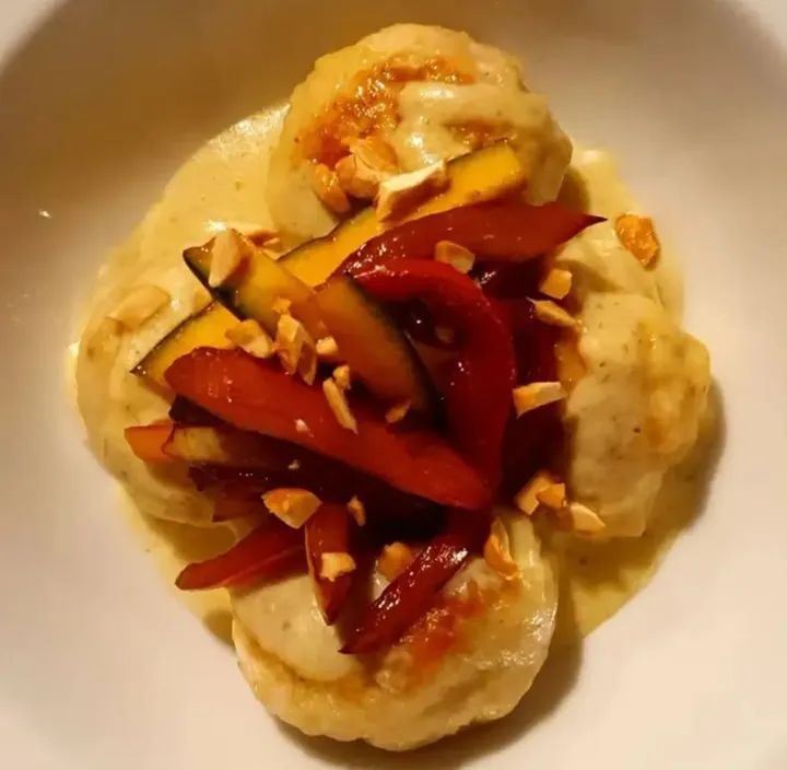 Polpette della Pecora Nera in crema gialla con peperoni rossi, zucca e frutta secca tritata su piatto bianco